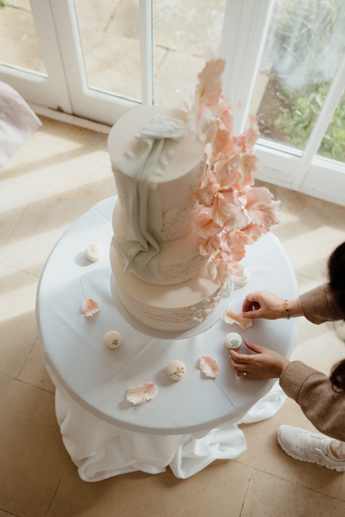 Arranging macarons around an elegant 3 tiered wedding cake showcasing Luxury wedding cakes.
