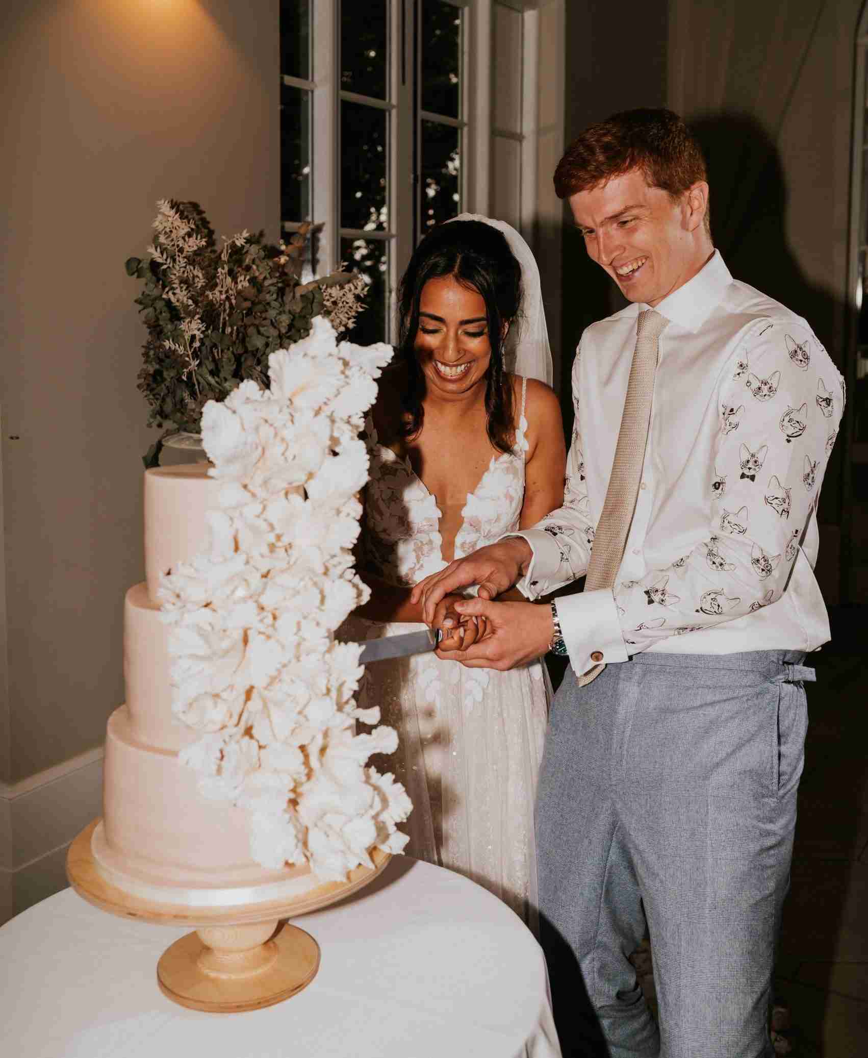 Bride and groom cutting a luxury white wedding cake adorned with cascading sugar flowers