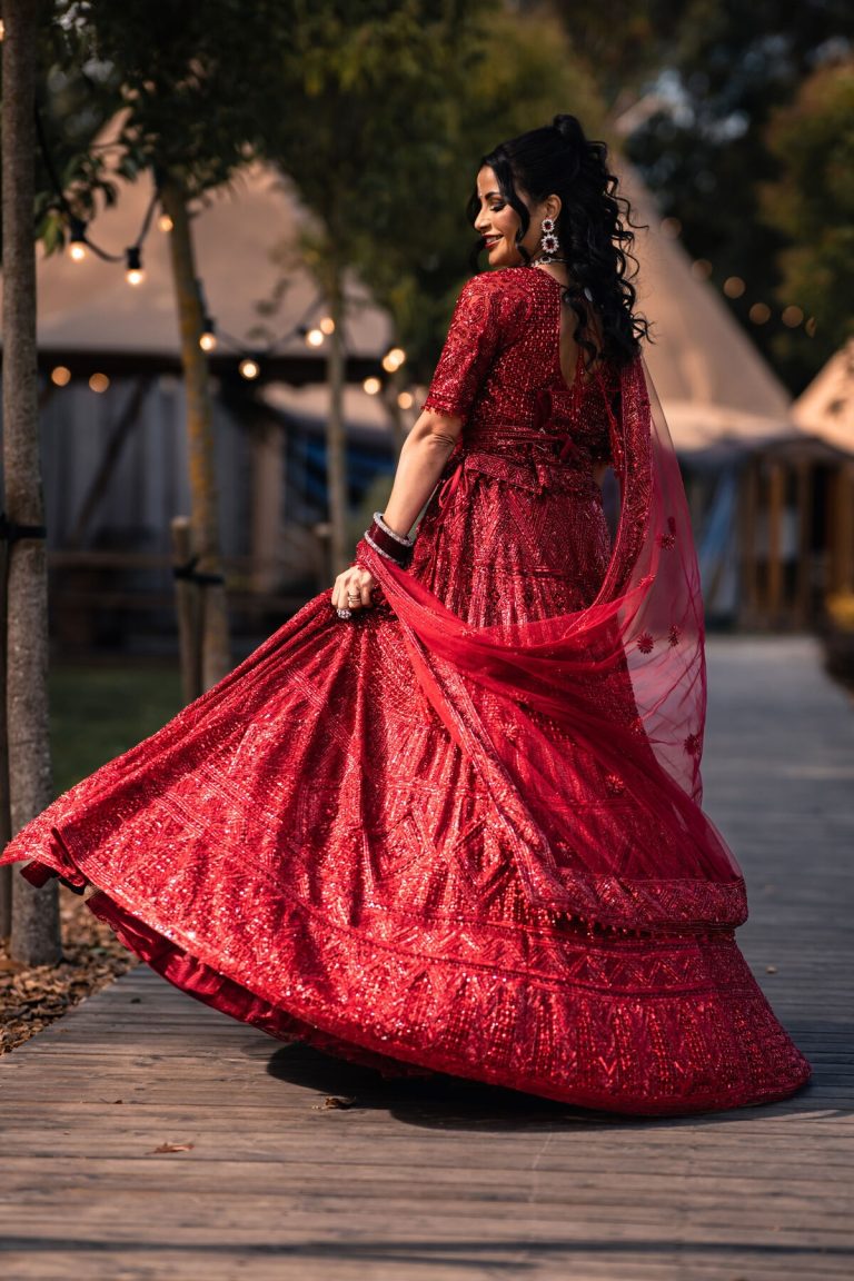 Bride twirling joyfully in her red Indian wedding outfit outside the tipi at The Hidden Hive wedding venue in the East Midlands.
