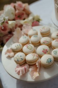 Elegant white macarons hand-painted with delicate pink and blue floral designs, beautifully arranged on a plate.
