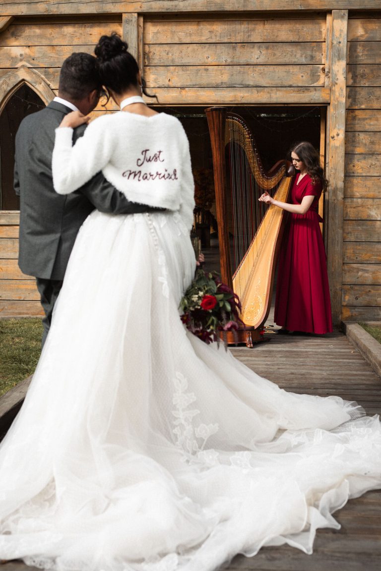 Newlywed couple peacefully watching a harpist perform soft music outside a rustic wedding barn in Leicestershire, East Midlands.