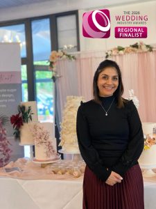 Luxury Wedding Cake designer Dimple from Sugar Creations by Dimple posing in front of her luxury wedding cakes, wearing a TWIA Regional Finalist badge for Best Wedding Cake Designer.