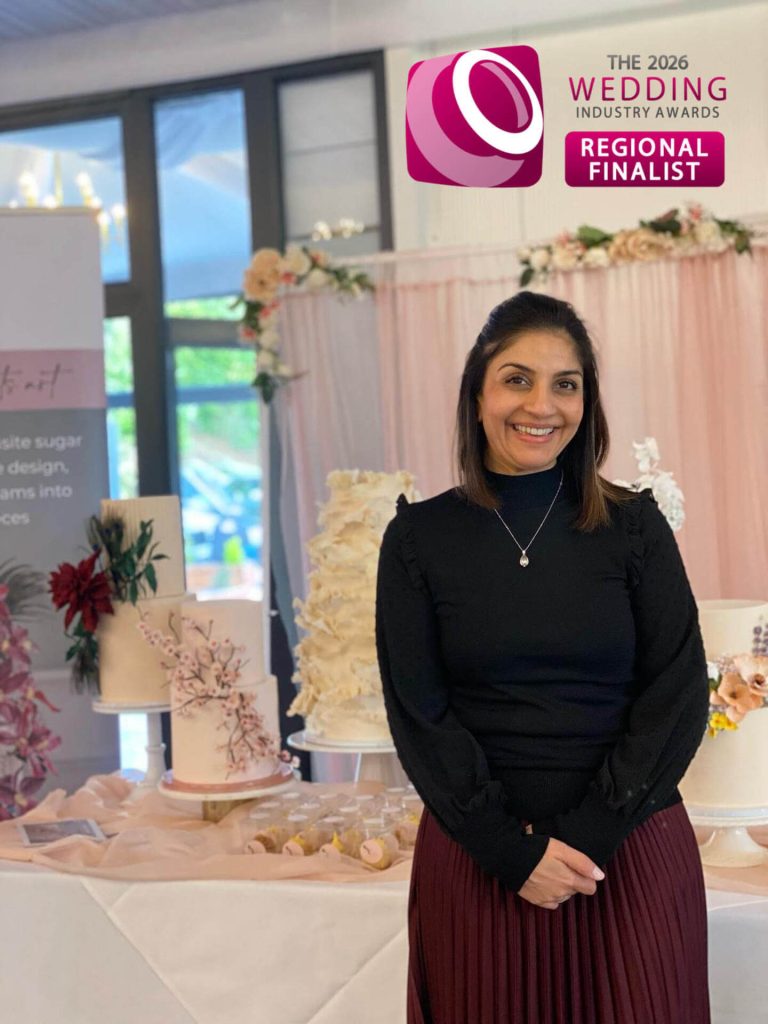 Luxury Wedding Cake designer Dimple from Sugar Creations by Dimple posing in front of her luxury wedding cakes, wearing a TWIA Regional Finalist badge for Best Wedding Cake Designer.