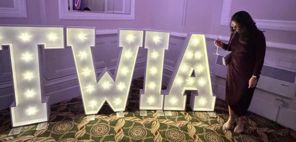 Dimple standing beside large illuminated TWIA letters at the Wedding Industry Awards event.