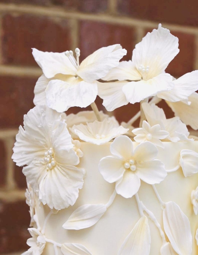 Close-up of the top tier of Grace and Dan’s luxury wedding cake featuring delicate handmade ivory sugar flowers and pearl detailing, created by Sugar Creations by Dimple in Leicestershire.