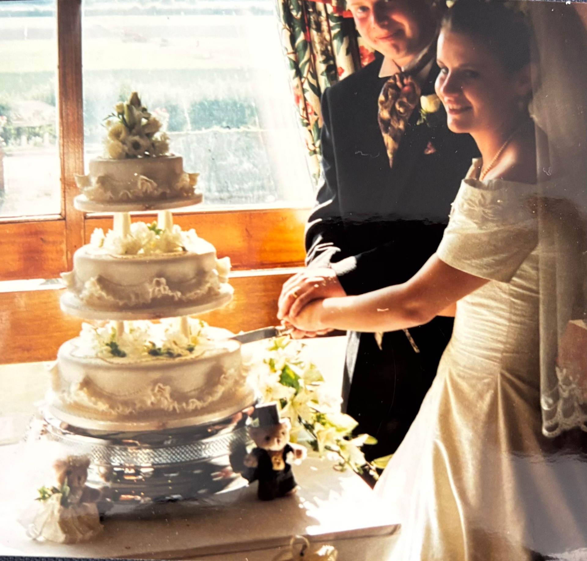 A photo of Grace’s parents cutting their wedding cake in 1995 with two teddy bears placed proudly in front — the same sentimental bears Grace used beside her own luxury wedding cake.