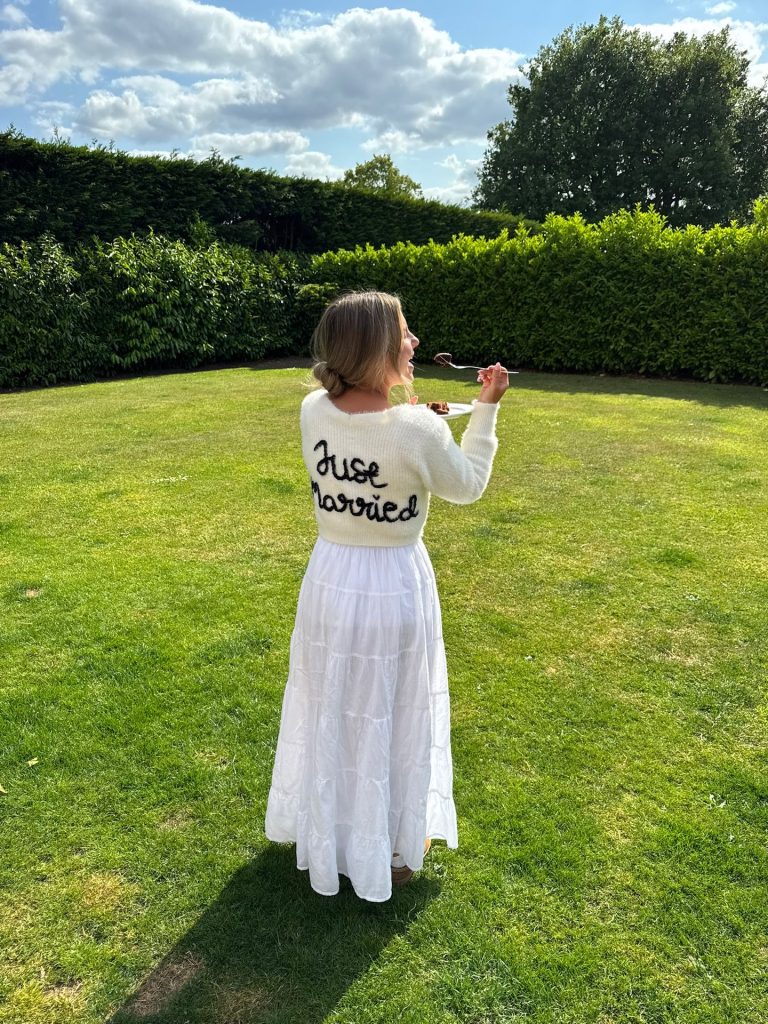 Grace wearing her “Just Married” cardigan enjoying a slice of her luxury wedding cake by Sugar Creations by Dimple at her Kilworth House wedding in Leicestershire.