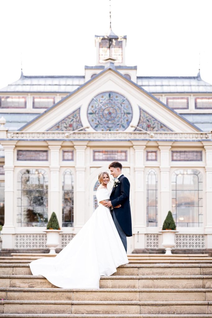Grace and Dan standing outside Kilworth House in Leicestershire on their wedding day, celebrating with their luxury wedding cake created by Sugar Creations by Dimple.